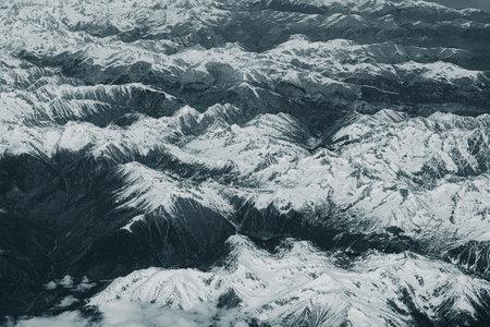 Aerial view of high rocky mountains covered with snow. Alpine landscape. Beauty in nature. Inaccessible mountain peaks. Harsh climate. Looking at the Earth from an airplane window. Aerial view of the landの写真素材