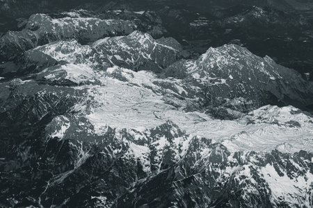 Aerial view of high rocky mountains covered with snow. Alpine landscape. Beauty in nature. Inaccessible mountain peaks. Harsh climate. Looking at the Earth from an airplane window. Aerial view of the landの写真素材
