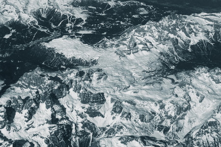 Aerial view of high rocky mountains covered with snow. Alpine landscape. Beauty in nature. Inaccessible mountain peaks. Harsh climate. Looking at the Earth from an airplane window. Aerial view of the landの写真素材