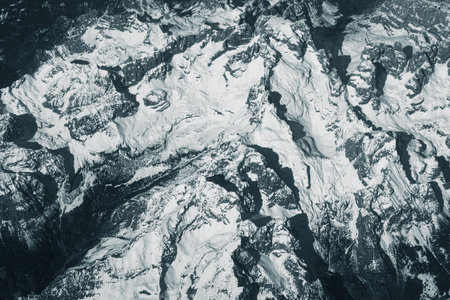 Aerial view of high rocky mountains covered with snow. Alpine landscape. Beauty in nature. Inaccessible mountain peaks. Harsh climate. Looking at the Earth from an airplane window. Aerial view of the landの写真素材