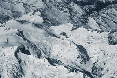Aerial view of high rocky mountains covered with snow. Alpine landscape. Beauty in nature. Inaccessible mountain peaks. Harsh climate. Looking at the Earth from an airplane window. Aerial view of the landの写真素材