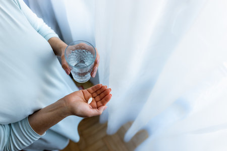 Adult woman holding a pill and a glass of water. Female taking medicine. Treating at home. Patient recovering in a hospital. Mental health. Migraine, diabetes, painkiller, influenza, headache, illness, sickness, depression and healthcare conceptの写真素材