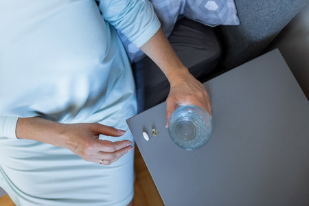 Adult woman holding a pill and a glass of water. Female taking medicine. Treating at home. Patient recovering in a hospital. Mental health. Migraine, diabetes, painkiller, influenza, headache, illness, sickness, depression and healthcare conceptの写真素材