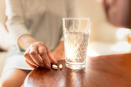 Adult woman holding a pill and a glass of water. Female taking medicine. Treating at home. Patient recovering in a hospital. Mental health. Migraine, diabetes, painkiller, influenza, headache, illness, sickness, depression and healthcare conceptの写真素材