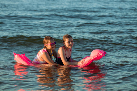 Children playing by the shore of the Baltic Sea in Poland. Girls playing in the water during summer vacation. Family holiday by the sea. Active leisure time. Joyful summer moments. Playing with inflatable toyの写真素材