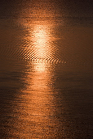 Morning on sea coast, red sun is relfected in waterの写真素材