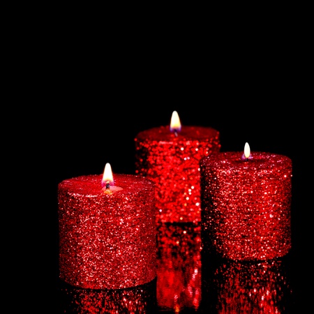Three red spangled candles isolated on black background. Shallow DOF, focus on the first candleの写真素材