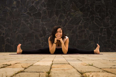 Beautiful young woman with curly hair sitting on split and smiling. Yoga posturesの写真素材
