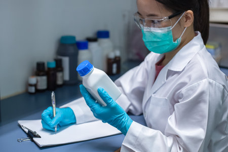 Chemical Research Laboratory; female scientist is reading the chemical label, chemical formula, and molecular weight to prepare the solution in the experiment. Research for pharmaceutical, medicine, and biotechnology development.の写真素材