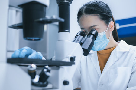 Female researcher use the inverted microscope to look at culture cells on a slide for bioassay of drugs test in the laboratory. Research for pharmaceutical, medicine, and biotechnology development.の写真素材
