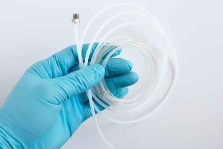A scientist's hand in a blue glove holds flexible PEEK tubing with a stainless steel fitting. This is a component for an HPLC liquid chromatography system in a lab.の写真素材