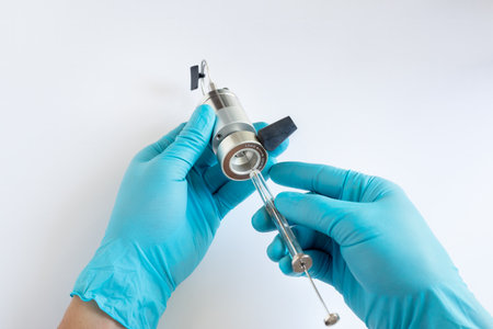 A scientistâs gloved hands demonstrate loading a liquid sample into a manual HPLC injection valve using a glass microsyringe with the valve in the LOAD position.の写真素材