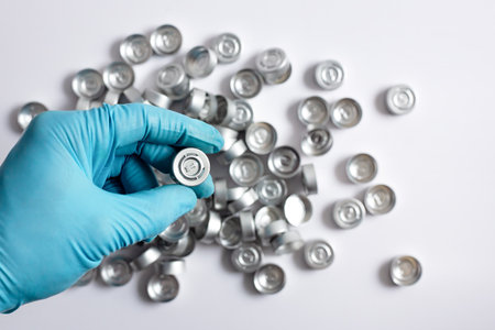 A scientistâs hand holds an aluminum vial cap used in laboratory sample preparation, with additional aluminum caps blurred in the background.の写真素材