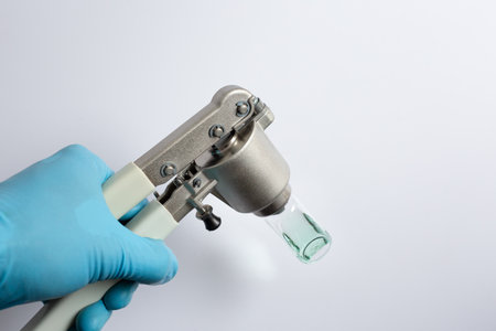 scientist's hand using a manual vial crimper tool to seal an aluminum cap onto a glass autosampler vial containing a green liquid sample. A step in sample preparation for gas chromatography (GC).の写真素材