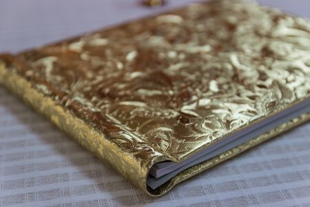 book with golden hardcover with flower tracery on white tableclothの写真素材