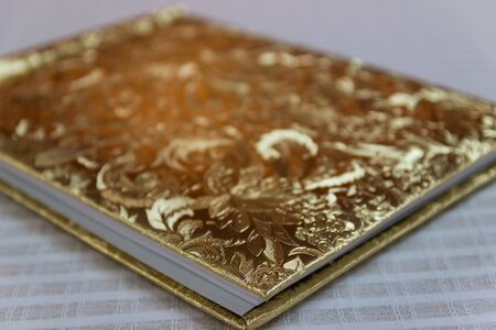 book with golden hardcover with flower tracery on white tableclothの写真素材