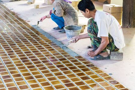 Uttaradit, Thailand - December 19, 2014: The worker is laying brown ceramic tile on the floor in Lomyen shop.のeditorial素材