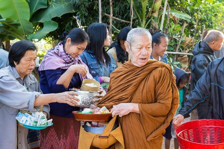 Sakon Nakhon, Thailand - December 21, 2014: People offer food on buddhist monk alms bowl in Sakon Nakhon, Thailand on December 21, 2014.のeditorial素材