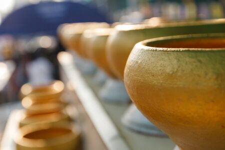 row of golden buddhist monk alms bowl for people to donate money in templeの写真素材