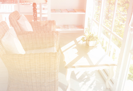 rose in vase on wooden table and rattan armchair with fabric cushion and pillow near the window with garden view (color filter and soft focus)の写真素材