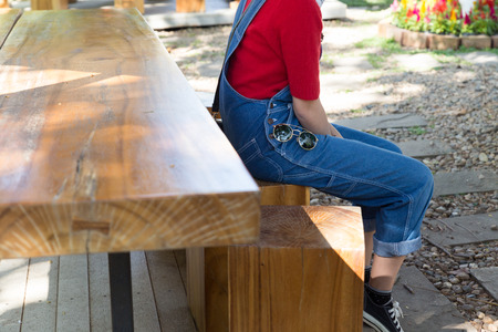 girl wearing red T-shirt and blue jeans with sunglasses sitting on wooden stoolの写真素材