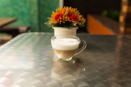 cup of cappuccino coffee and artificial orange flower on metal tableの写真素材
