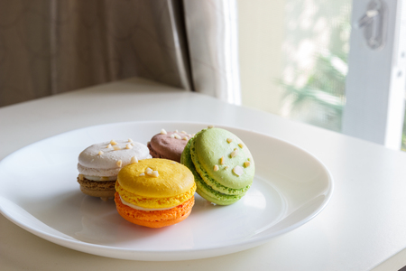 orange, white, brown green macaroon on white plateの写真素材