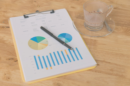 pen, business document and and empty coffee cup on wooden table (vintage tone and color filter)の写真素材