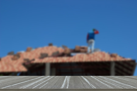 man work on tile arrangement on home roof construction (blur background and wooden table for displaying your product)の写真素材