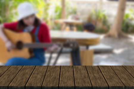 girl wearing red T-shirt and blue jeans sitting on wooden stool and playing guitar (blur background with wood table top for display or montage your product)の写真素材