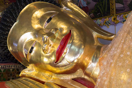smiling face of reclining golden buddha statue in asian templeの写真素材