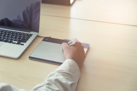 man' hand holding pen working on digital tablet and computer notebook for graphic design work, vintage toneの写真素材