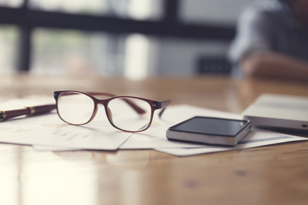 eyeglasses, business document and laptop computer notebook on wooden table, selective focus and vintage toneの写真素材
