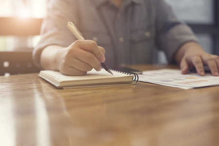 woman's hand writing on notebook with business document for working concept, selective focus and vintage toneの写真素材
