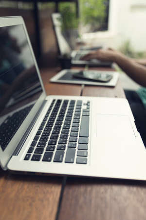 man's hand typing on laptop computer with smartphone and digital tablet on wooden table, selective focus and vintage toneの写真素材