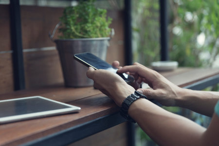 man's hand using smartphone with digital tablet on wooden table, selective focus and vintage tone