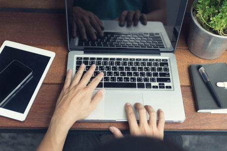 man's hand typing on laptop computer with smartphone and digital tablet on wooden table, selective...