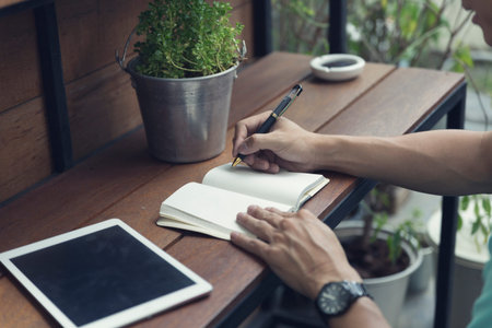 man writing on notebook with digital tablet on wooden table, selective focus and vintage tone