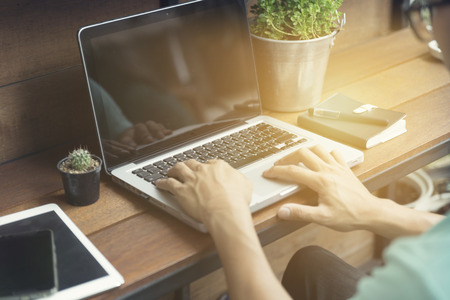man's hand typing on laptop computer with smartphone and digital tablet on wooden table, selective focus and vintage toneの写真素材