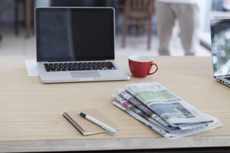 laptop computer, newspaper, notebook, pen and red coffee cup on wooden table for working conceptの写真素材