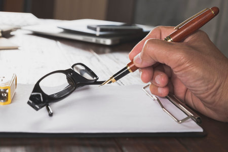 hand holding pen with notepad and eyeglasses on wooden office desk