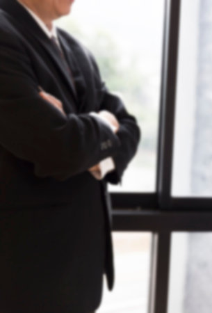 businessman in suit folded his arm standing beside office window - blur for use as backgroundの写真素材