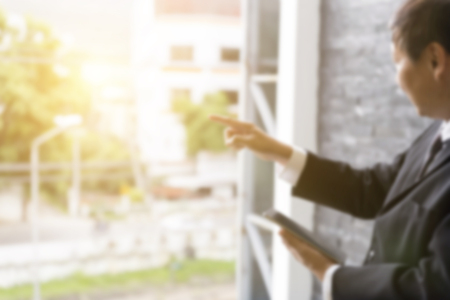 businessman holding tablet and pointing his finger out of window - blur for use as backgroundの写真素材
