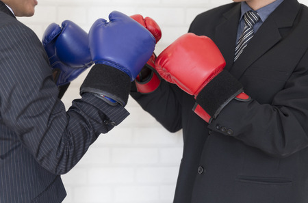 businessman in necktie and suit with red and blue boxing gloves punching each other - business competition conceptの写真素材