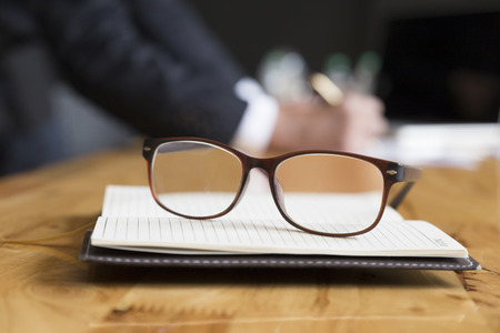 eyeglasses on notebook with background of businessman in suit working with document on office deskの写真素材