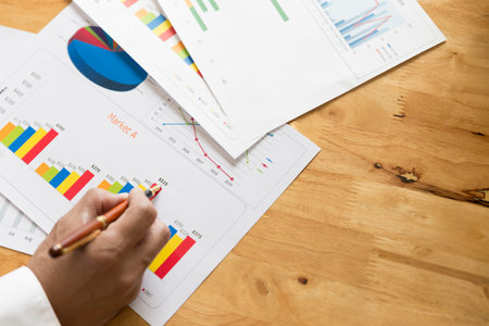 businessman hand holding pen with graph and chart analysis paperwork document on office desk