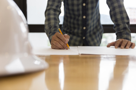architect holding pencil working on blueprint of construction project in workplace with computer on office deskの写真素材