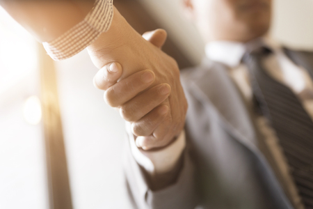 two businessman in suit shaking hands beside window - business teamwork, cooperation conceptの写真素材