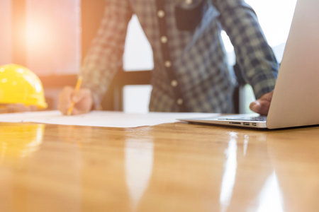 architect holding pencil working on blueprint of construction project in workplace with computer on...