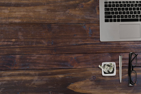 laptop computer, black eyeglasses, cactus pot and pen on wood office desk - top view